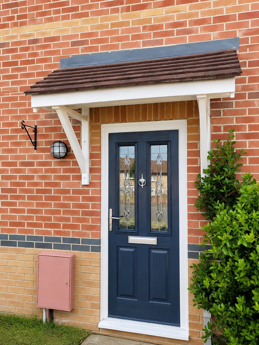 Navy blue composite front door with decorative leaded glazing under a tiled porch canopy on a red brick house