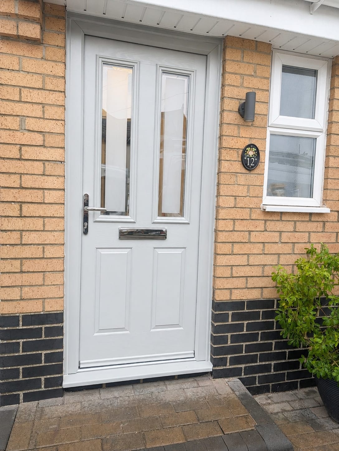 Light grey composite front door with two glazed panels and chrome letter plate in a brick porch