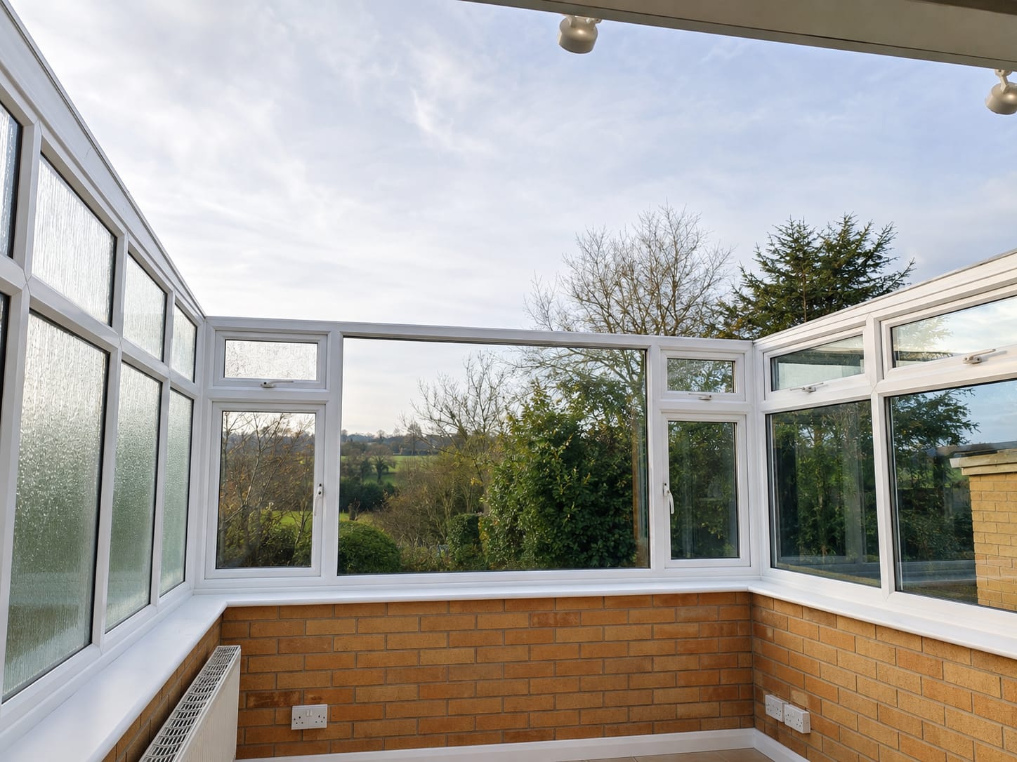Conservatory roof replacement after: bright interior with white UPVC windows over a brick dwarf wall and countryside views