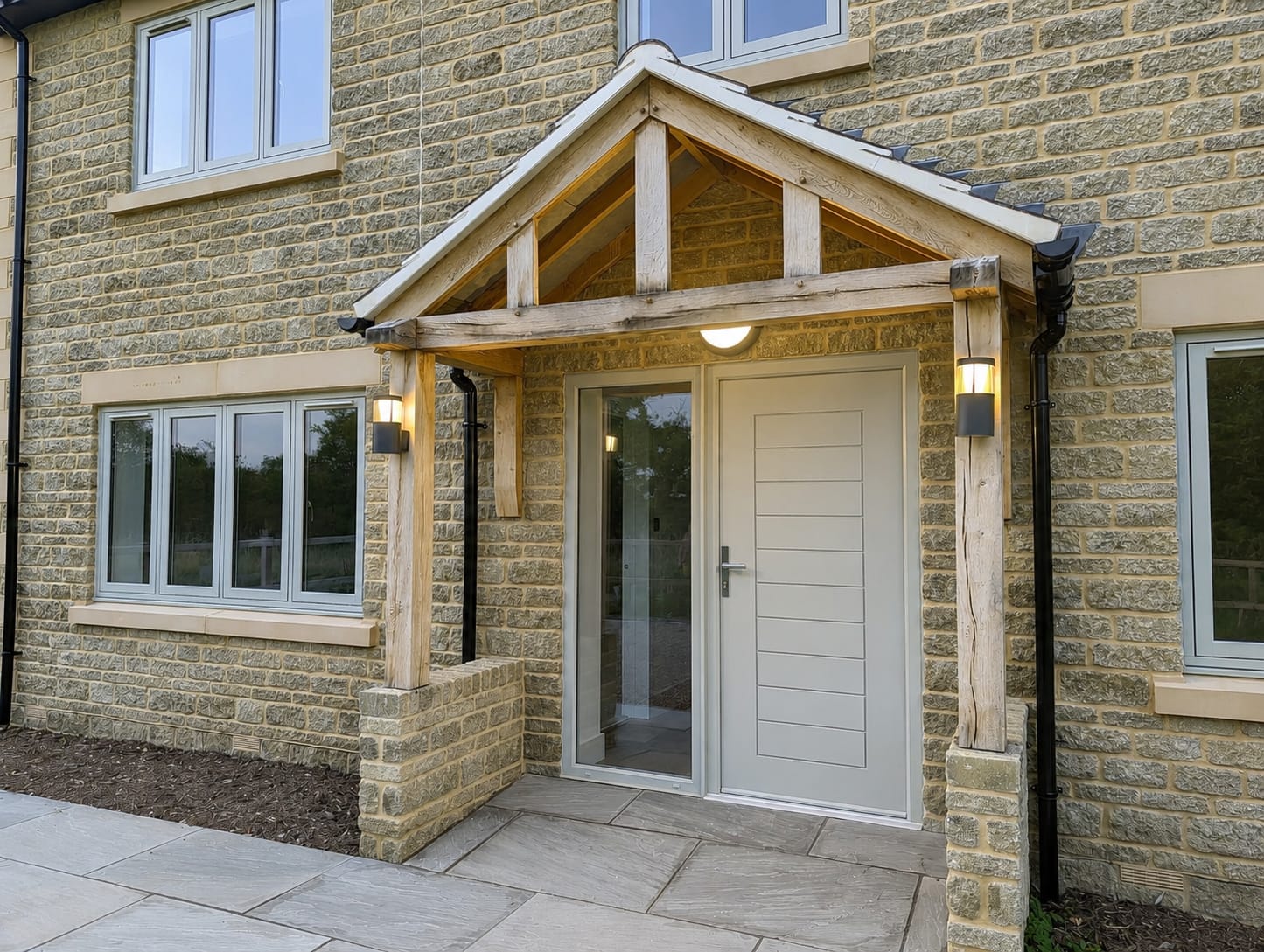 Cream composite front door with glazed side panel under an oak porch on a Cotswold stone house