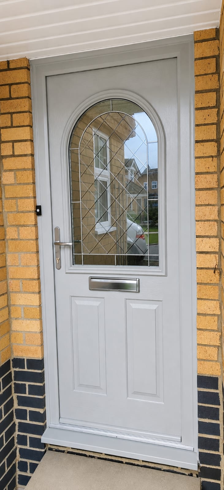 Light grey composite front door with arched leaded glass panel in a brick porch