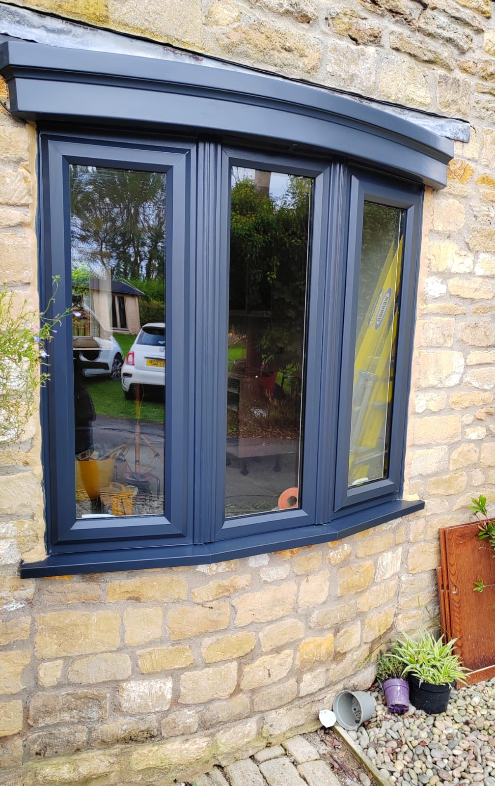 Anthracite grey UPVC bow window with matching lead canopy on a Cotswold stone cottage