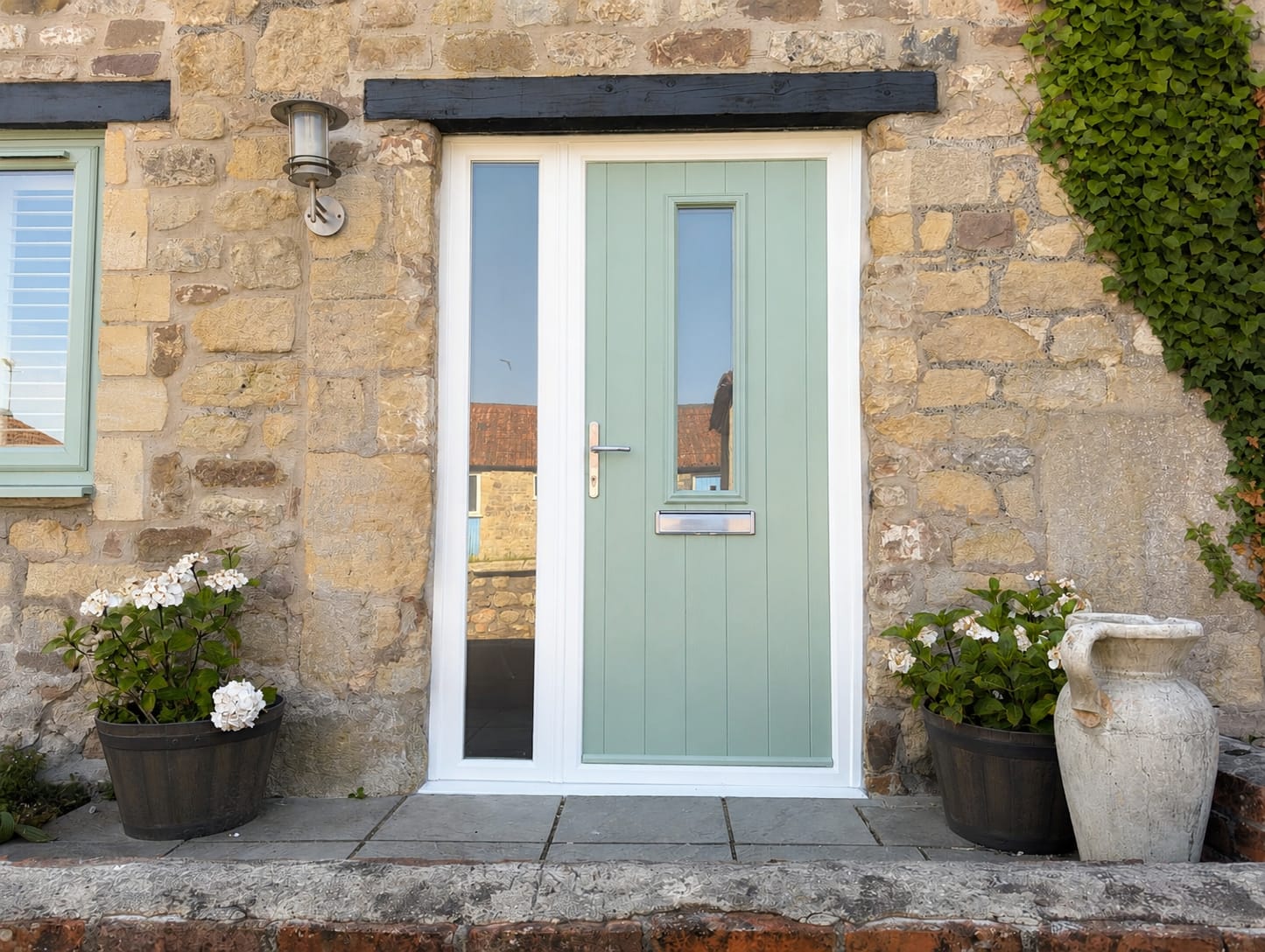Sage green composite front door with side window in a rustic stone cottage wall