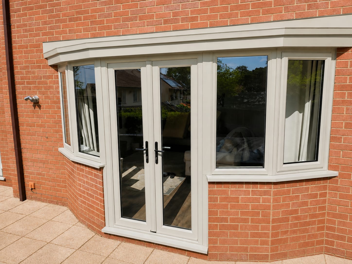 Light grey UPVC French doors set in a red brick bay with side casement windows