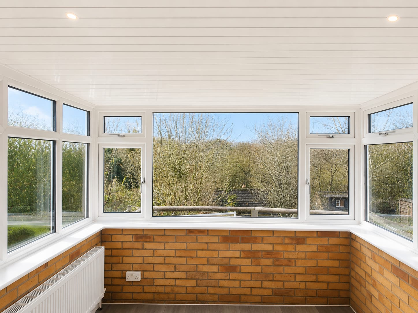 Conservatory roof replacement after: finished clad ceiling above white UPVC windows and brick dwarf wall with countryside views